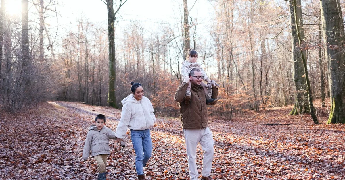 Une famille profitant d'une balade dans une forêt avec des feuilles mortes, capturant un moment chaleureux d'automne.