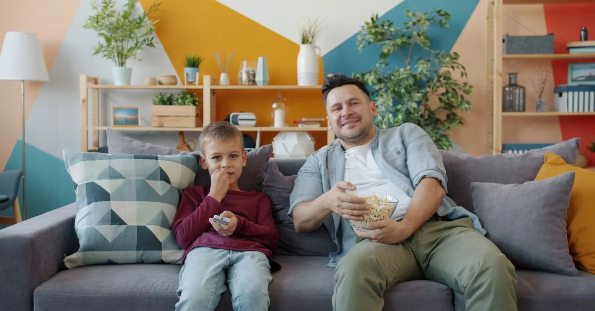 Un père et son fils savourent des en-cas sur le canapé d'un salon confortable.
