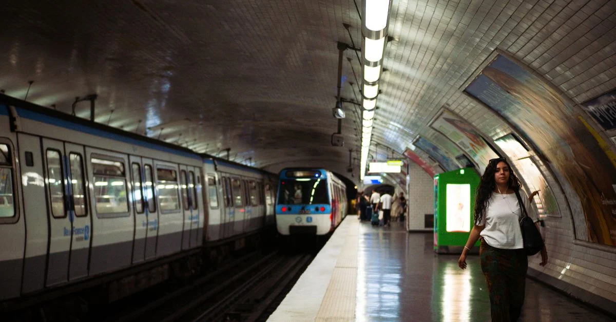 Une femme marche dans une station de métro parisienne faiblement éclairée, à côté d'un train à l'arrêt, capturant ainsi une scène de la vie urbaine.